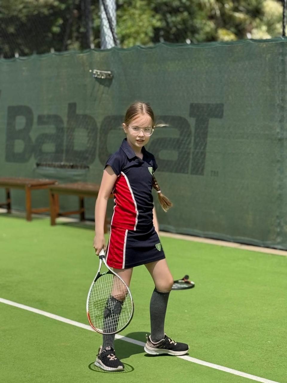 A pupil stands ready with her racket on the tennis court.