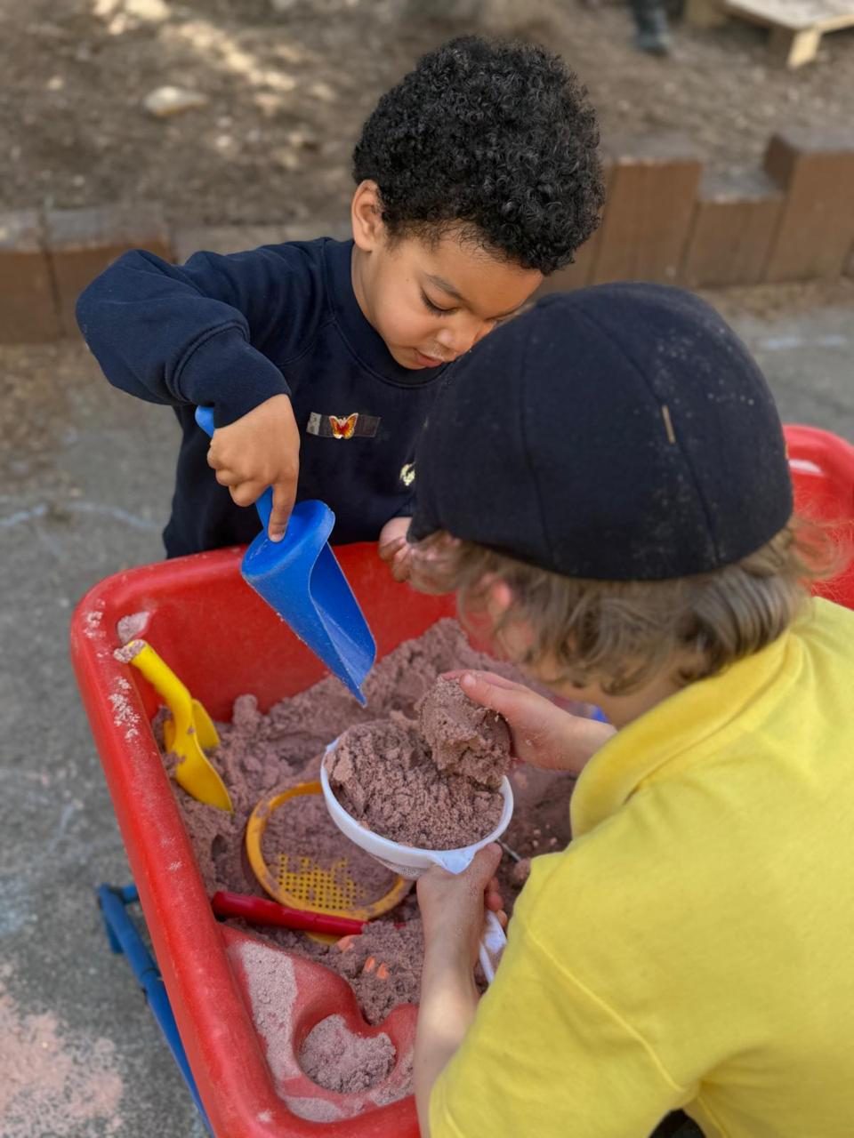 Two young children scoop and pour together at the sand tray.