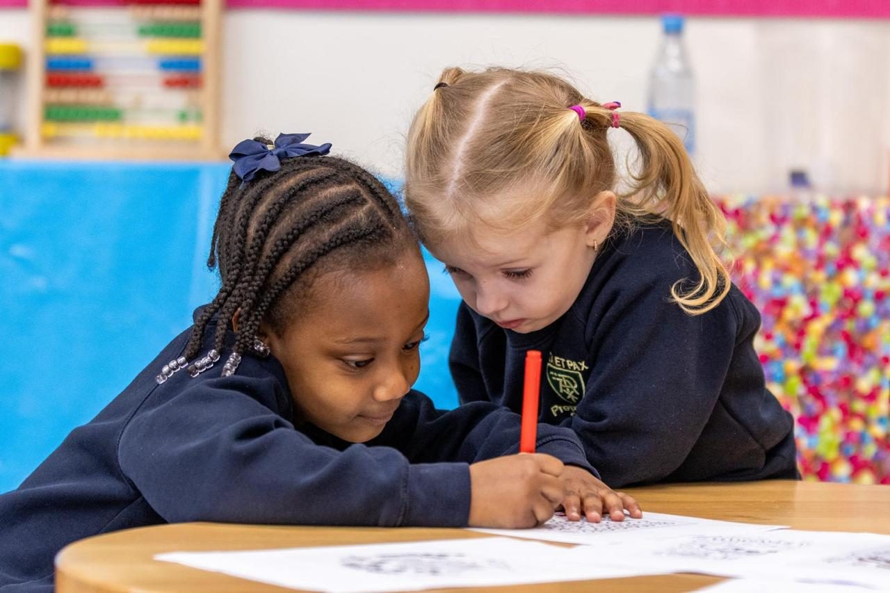 Two children practise their early writing at a classroom table.
