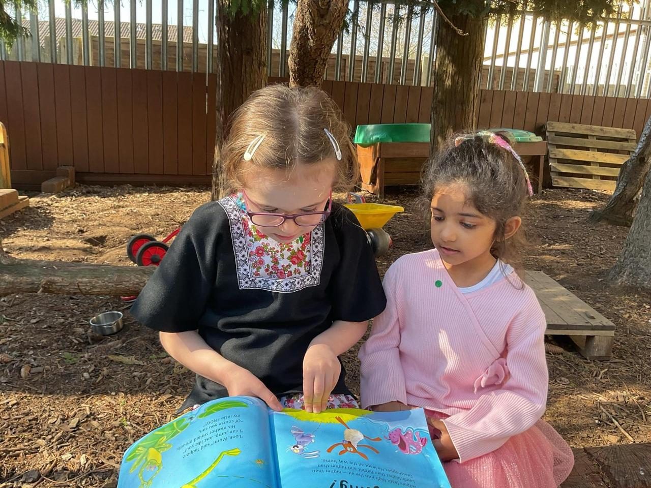 Two young children share a picture book together outdoors.