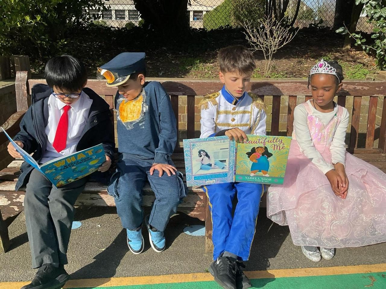 Four children in book-character costumes sit along a bench for World Book Day.