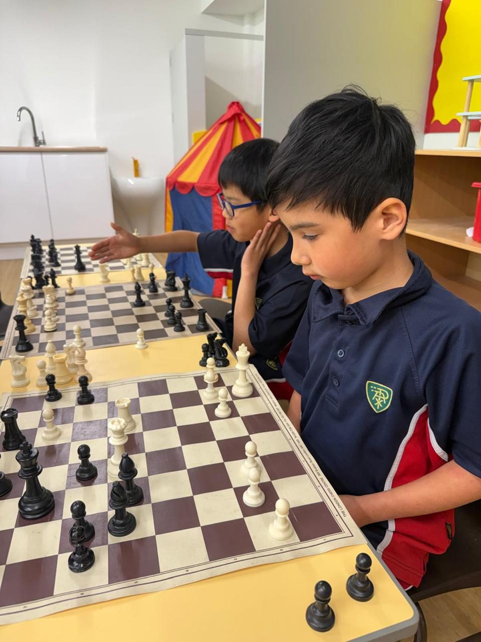 Two pupils face each other across their chess boards.