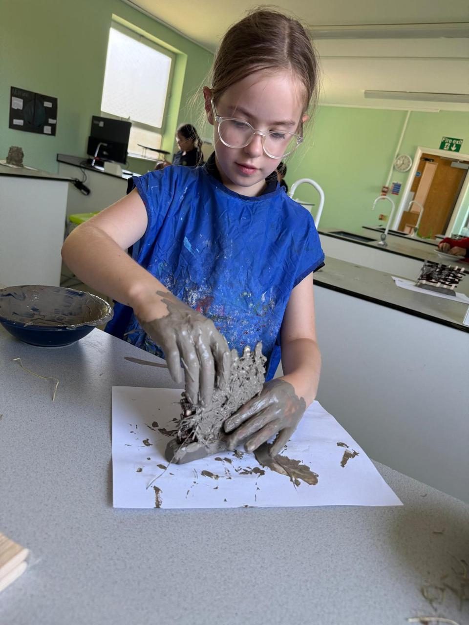A pupil in an apron works on a clay sculpture.