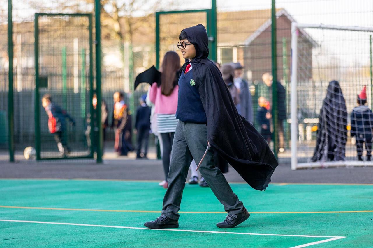 A pupil in a book-character cape striding across the playground on World Book Day