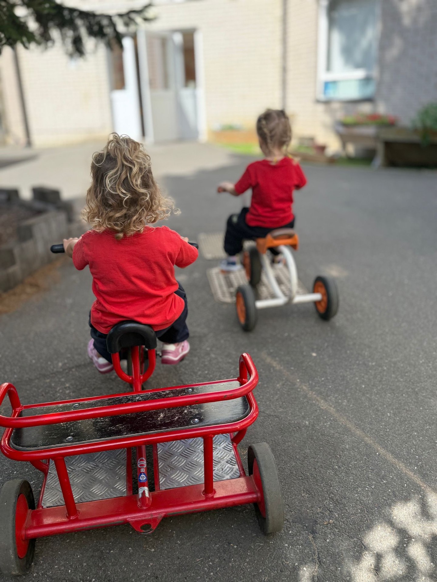 Nursery children riding tricycles in the outdoor play area at Vita et Pax Preparatory School, Southgate N14, North London